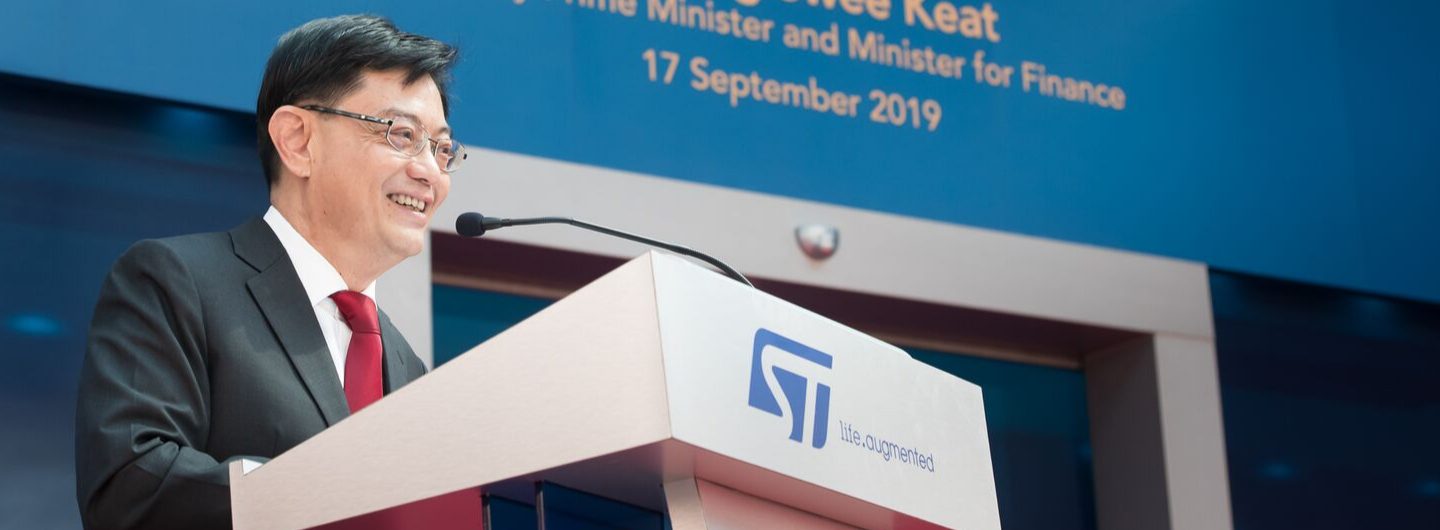 Man in suit at STMicroelectronics podium, microphone, blue backdrop with text.